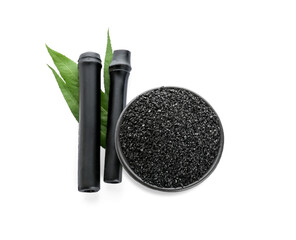 Bowl of activated carbon powder and black bamboo sticks isolated on white background
