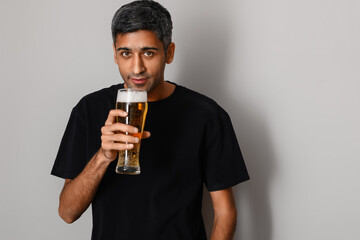 Handsome man drinking beer on light background