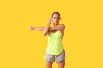 Sporty young woman stretching on yellow background