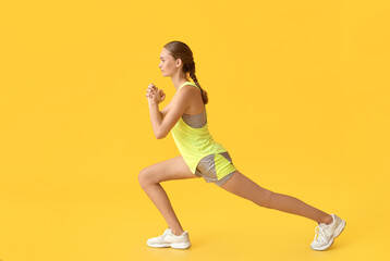 Sporty young woman exercising on yellow background