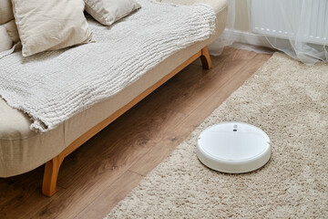 White robot vacuum cleaner on a fleecy carpet, home interior