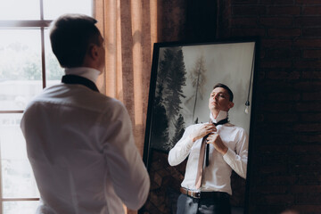 Morning of a stylish groom, man, in a black suit and tie, his preparations at the hotel, in a photo studio, fastening buttons and jacket, portraits