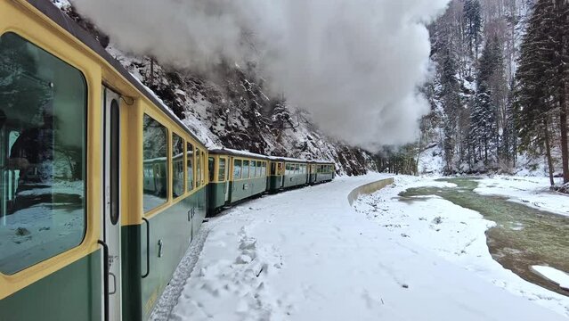 View of the moving steam train Mocanita from inside it, bare forest and river in winter, snow, filming passengers, Romania. Slow motion