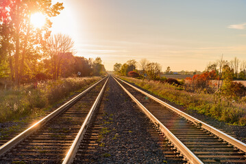 Railway tracks running through the countryside at sunset in autumn. Lens flare.