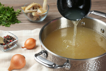 Delicious homemade bone broth and ingredients on wooden table, closeup