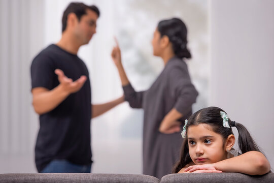 Sad girl baby looking elsewhere with resting her chin on hands while parent arguing behind