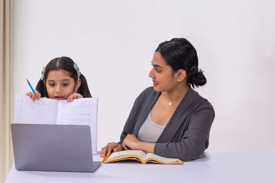 Girl submitting homework through online class using laptop and mother sitting beside