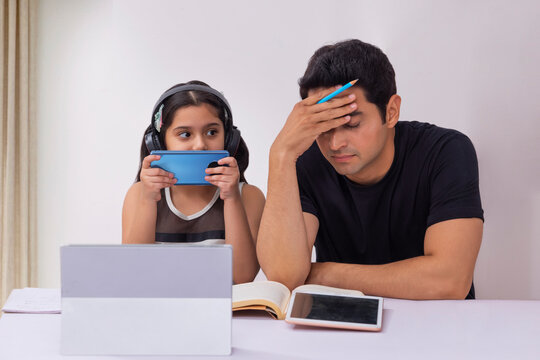 Girl listening music using smartphone and father thinking with hand on head under work pressure