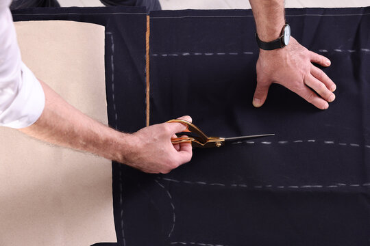 Professional tailor cutting fabric by following chalked sewing pattern at table, top view