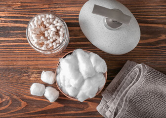 Bowl of cotton wool, swabs, towel and bottle of cosmetic product on wooden background