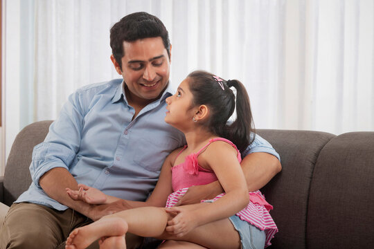 Father and daughter talking each other while sitting on sofa at home