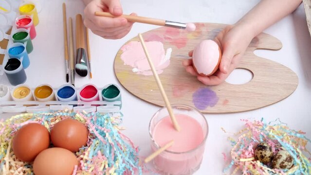 View from above. Easter preparation concept. Quail and chicken eggs, paints, brushes and a palette are laid out on the table. Children's hands paint eggs in pastel shades. happy easter