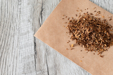 Dried marijuana on a handful lying on a piece of paper on a wooden background. Dried tobacco on the...