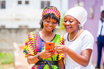 image of two beautiful african ladies with smart phone- black women enjoying social media outside- communication concept