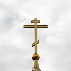 Square photo of an Orthodox cross in cloudy weather against the sky.