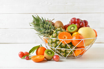 Basket with juicy fruits on white wooden background