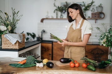 Pretty woman with green ingredients thinking about cooking healthy food on the kitchen. Healthy and wellness concept