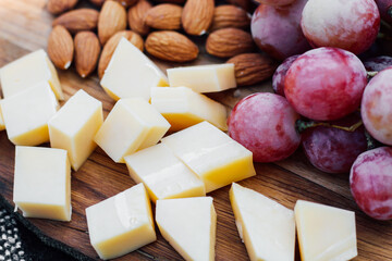 Wooden board with fruits, cheese, nuts, picnic snacks.