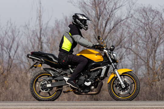 A motorcyclist on a yellow road bike rides on the track in cloudy weather at the end or beginning of the season.