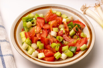 Tomato and spring onion relish in lemon juice in a china bowl, white background.