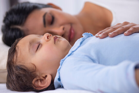 Close-up portrait of sleeping baby and mother lying beside on bed
