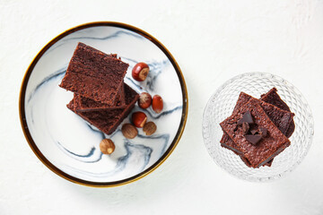 Plate and bowl with pieces of tasty chocolate brownie on light background