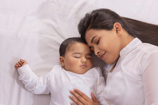 Mother caressing her sleeping baby with affection while lying beside