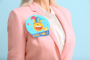 Mature woman with paper attached to her clothes on blue background. April fools day celebration