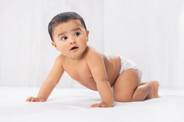 Cute baby in diaper crawling on bed