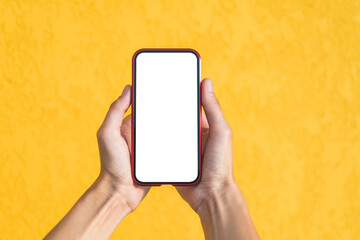 Mockup of a red smartphone in the hands of a girl. Against the background of a yellow facade made of decorative plaster.
