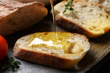 Pouring oil onto slices of bread on wooden plate, closeup