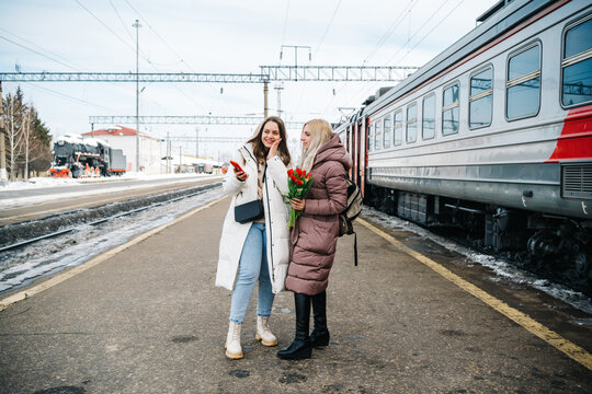 two girls on the station platform with flowers happily looking into a smartphone
