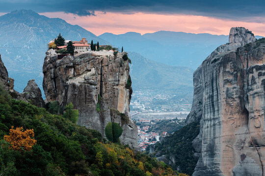 Scenic twilight view of the Monastery of the Holy Trinity in Meteora at sunset and Kalambaka town at the distance. Tourist and pilgrimage experience. Natural and religious wonders of Greece.