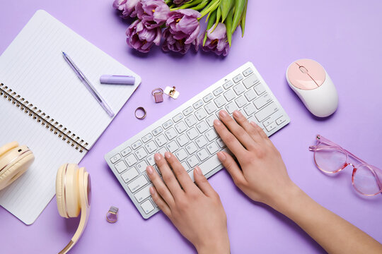 Female hands with keyboard, flowers, accessories and notebook and lilac background