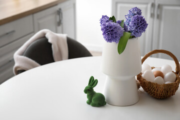 Vase with fresh hyacinth flowers, figurine of bunny and basket with eggs on table in kitchen. Easter celebration