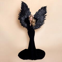 Elegant fashion. Stunning blonde woman in elegant long black dress and big wings on beige...