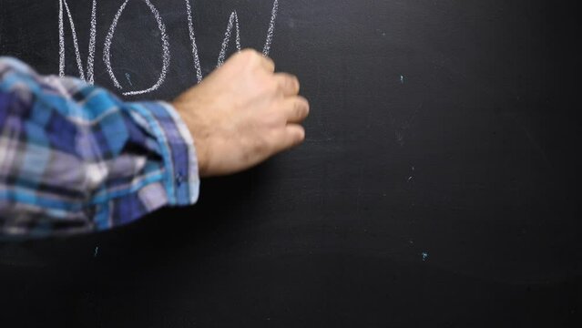 A man's hand in a plaid shirt writes NO WAR with chalk on the black board and draws the Ukrainian flag. A protest against the war in Ukraine