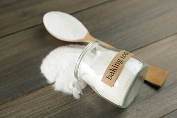 Overturned jar and spoon with baking soda on wooden table, closeup