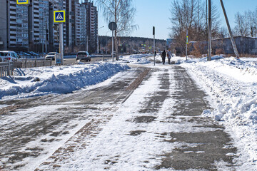 Pedestrians walk along a snow-covered sidewalk on a sunny spring day