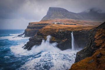 Dramatic view of Mulafossur waterfall with Gasadalur village on background. Vagar island, Faroe Islands, Denmark. November 2021.