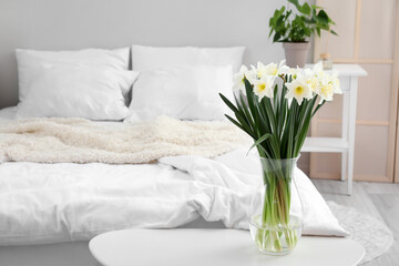 Fototapeta na wymiar Vase with daffodils on table in light bedroom