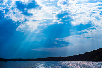 The rays of God in the river landscape. The sun's rays shine through the clouds over the water surface and the shore. Copy space