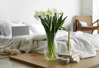 Vase with daffodils, books and candles on board in bedroom