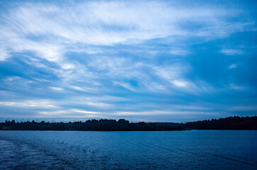 River landscape. Calm water and blue sky with clouds. Trees grow on the nearest shore. There is copy space
