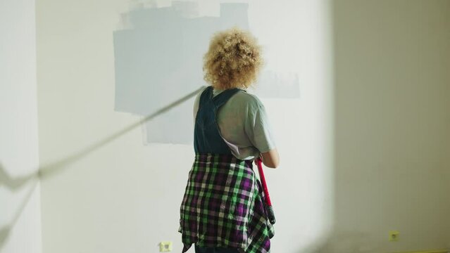 Curly hair Woman from behind is painting wall in gray using paint rollers. slowmotion