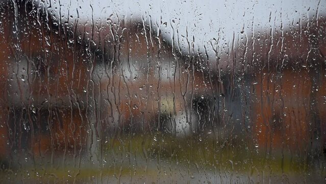 Close up of window pane during rainfall with water streaks and blurred houses in background