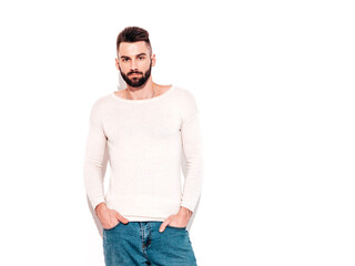 Portrait of handsome confident stylish hipster lambersexual model.Man dressed in white sweater and jeans. Fashion male posing near white wall in studio. Isolated