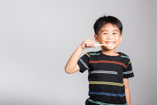 Little Cute Kid Boy 5-6 Years Old Brushing Teeth And Smile In Studio Shot Isolated On White Background, Happy Asian Children Holding Toothbrush In Mouth By Himself, Dental Hygiene Healthy Concept