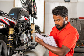 mechanic busy noting down bike repair parts during maintenance repair at grage for customer billing - concept of professional occupation,repair man and skill labor.