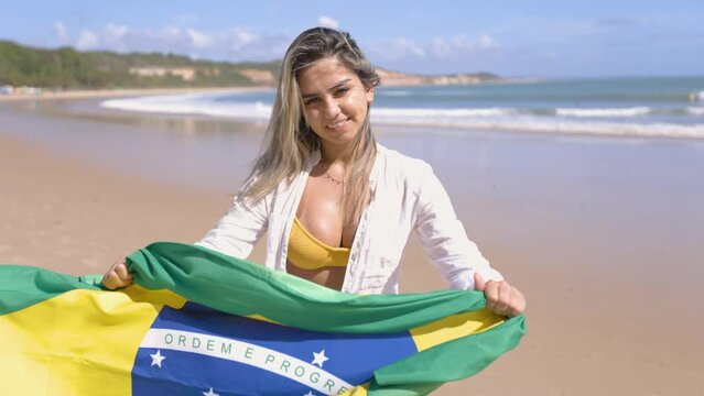 latin woman with brazil flag celebrating, in a beach setting. Large northern river. Madeiro Beach. Supporter of the Brazilian team.